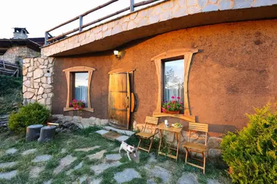 a dog standing outside of a house with a table and chairs at Панорама хаус Лещен и еко къщи Дървена и Землянка in Leshten
