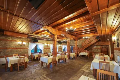 a restaurant with tables and chairs and wooden ceilings at Hotel Leshten in Leshten
