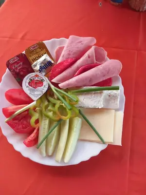 a plate of meats and vegetables on a red table at Стаи за гости - Цветето на Ангела in Bankya