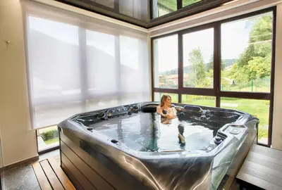 a woman sitting in a hot tub in a room with windows at MOUNTAIN HILL LUXURY VILLA in Madzhare