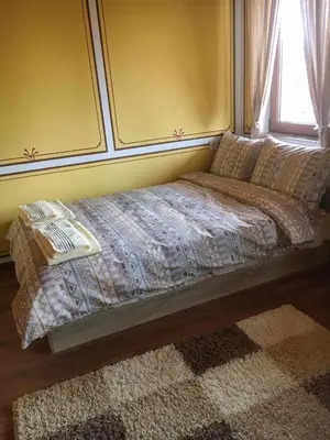 a bed in a bedroom with a window and a rug at Стаи за гости Бащино огнище in Koprivshtitsa