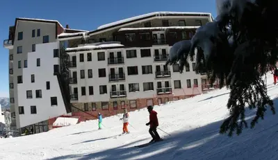 three people skiing down a snow covered slope in front of a building at Студио, хотел Стената in Pamporovo