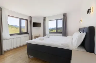 a bedroom with a large bed with two windows at Вила ИГЛИКА in Yagodina