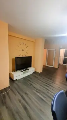 a living room with a tv and a clock on the wall at Елегантен градски апартамент с обширна тераса in Pernik
