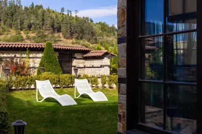 two white chairs sitting in the grass near a window at Armaco Residence in Koprivshtitsa