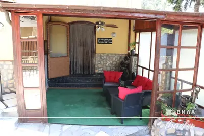 a porch of a house with two couches and red pillows at ВИЛА БАЕВИ in Velingrad