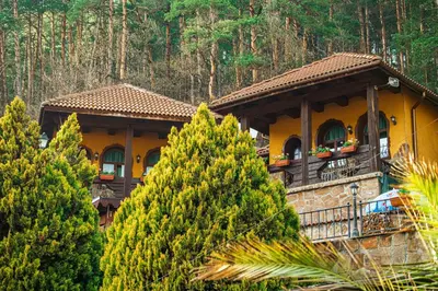 a yellow house with a balcony and some trees at Safari Village Velingrad in Velingrad