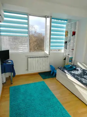 a bedroom with a bed and a desk and two windows at Alinik Apartment in Sofia