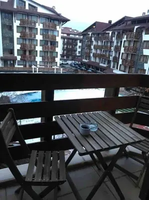 a wooden table and chair on a balcony with buildings at Lovely private apartment in Belelvedre in Bansko
